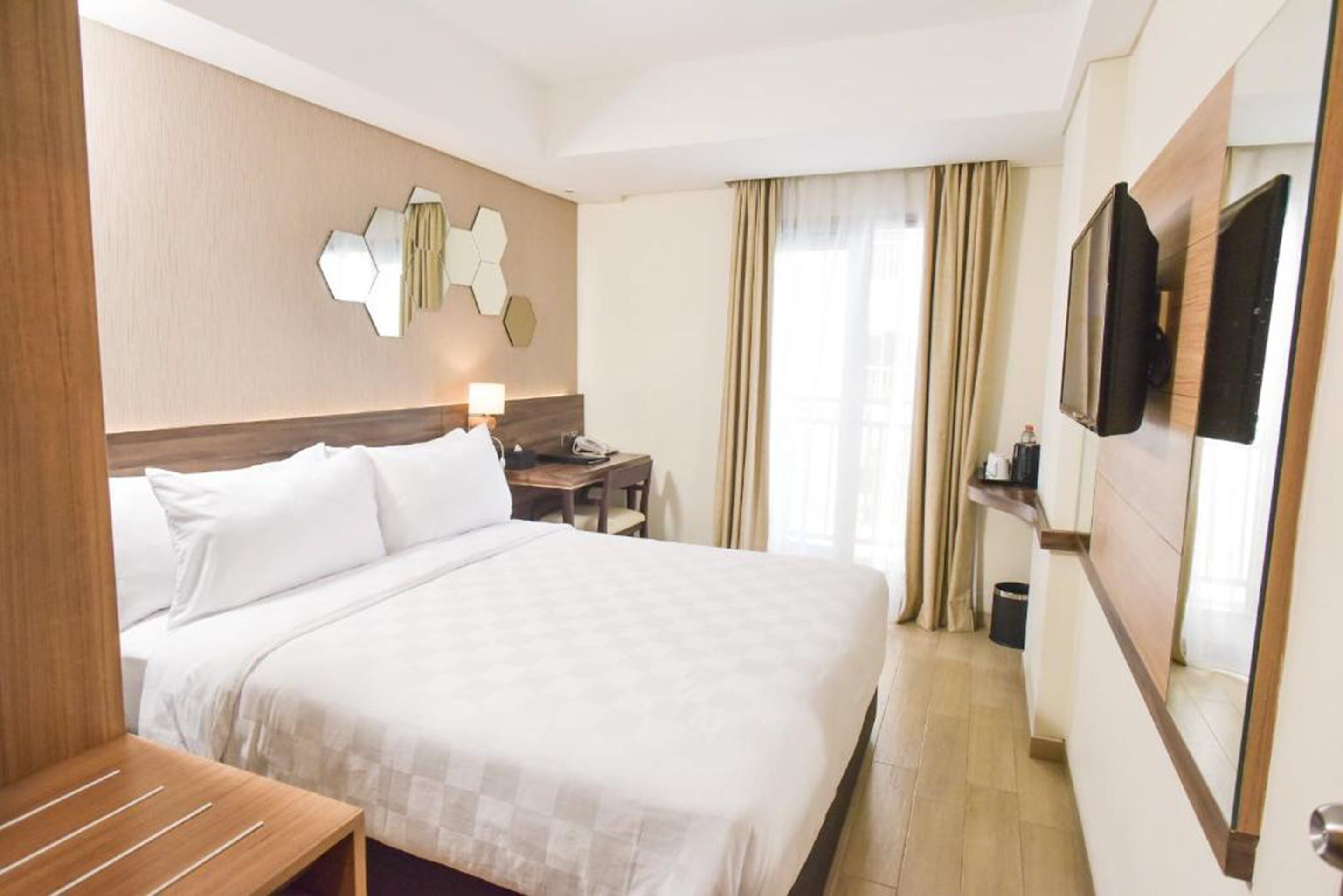 Habitación de hotel con una cama grande, un escritorio, una silla, un televisor y un espejo.