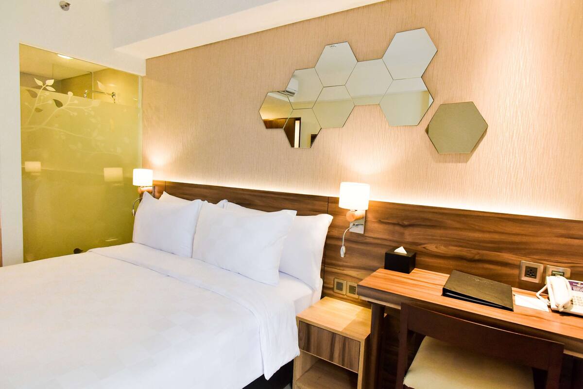 A hotel room with a large bed, bedside tables, a desk, and a wall-mounted mirror.