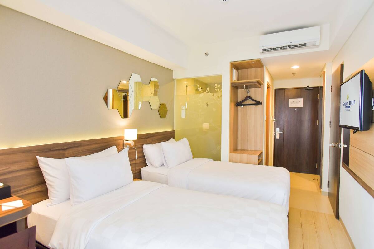 A hotel room with two beds, a wooden headboard, a mirror, a TV, and a wardrobe.