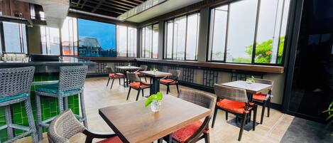 A restaurant with wooden tables and chairs, large windows, and a view of the city.