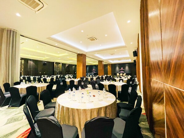Un amplio salón de banquetes con mesas redondas, sillas negras y un alto techo con iluminación empotrada.