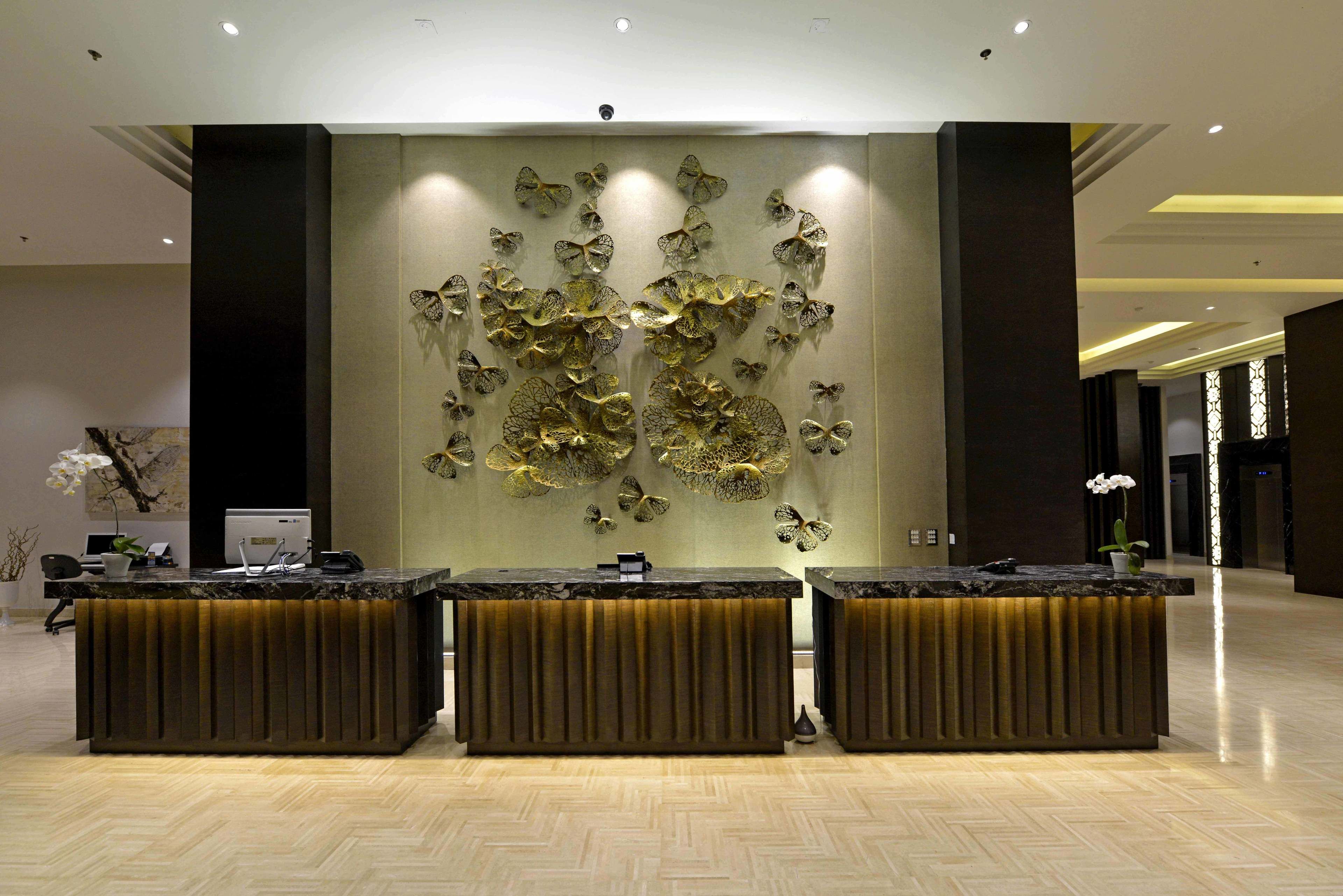 Un área de recepción con tres mostradores, un panel decorativo en la pared y una planta en maceta.