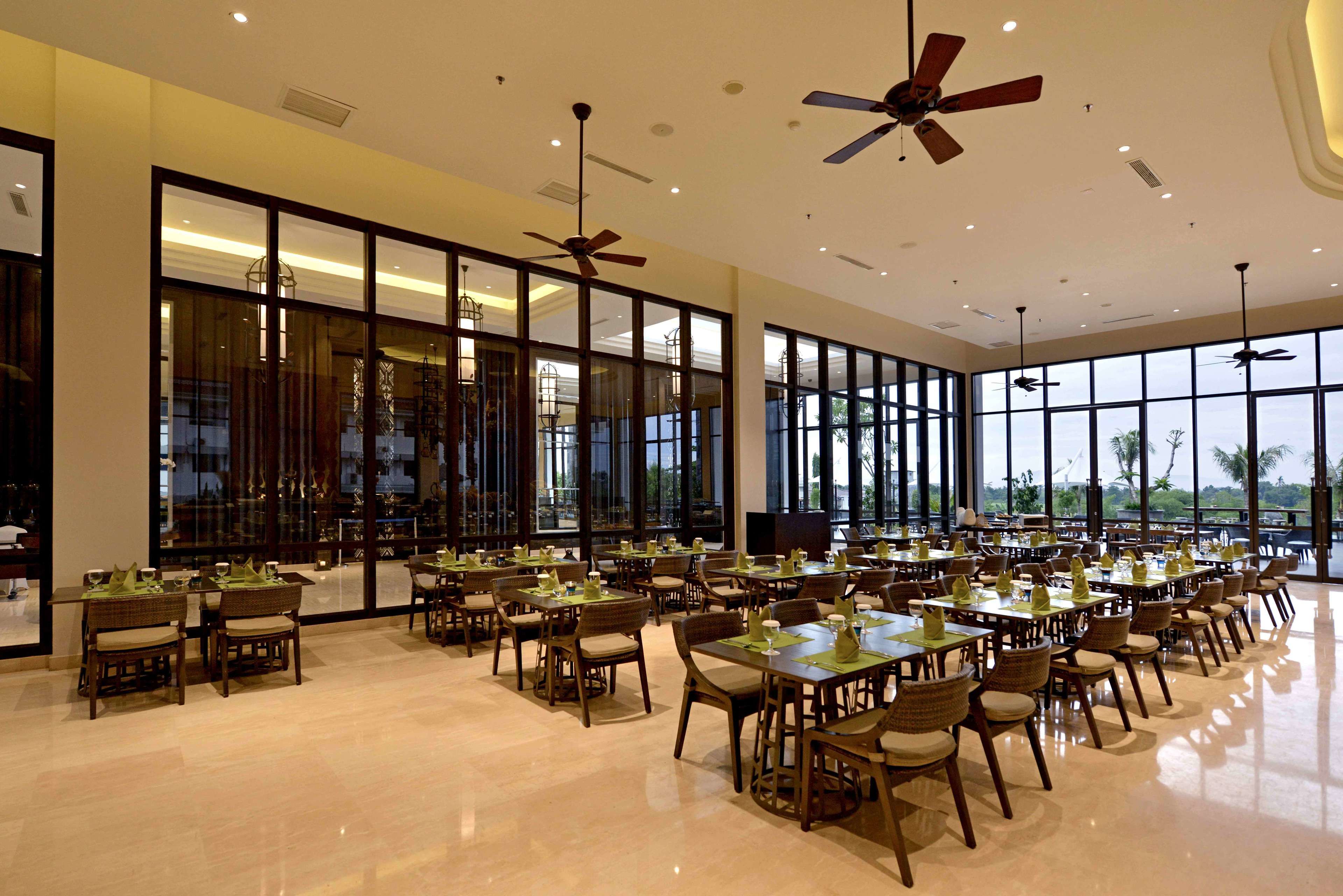 A spacious dining area with multiple tables and chairs, large windows, and ceiling fans.