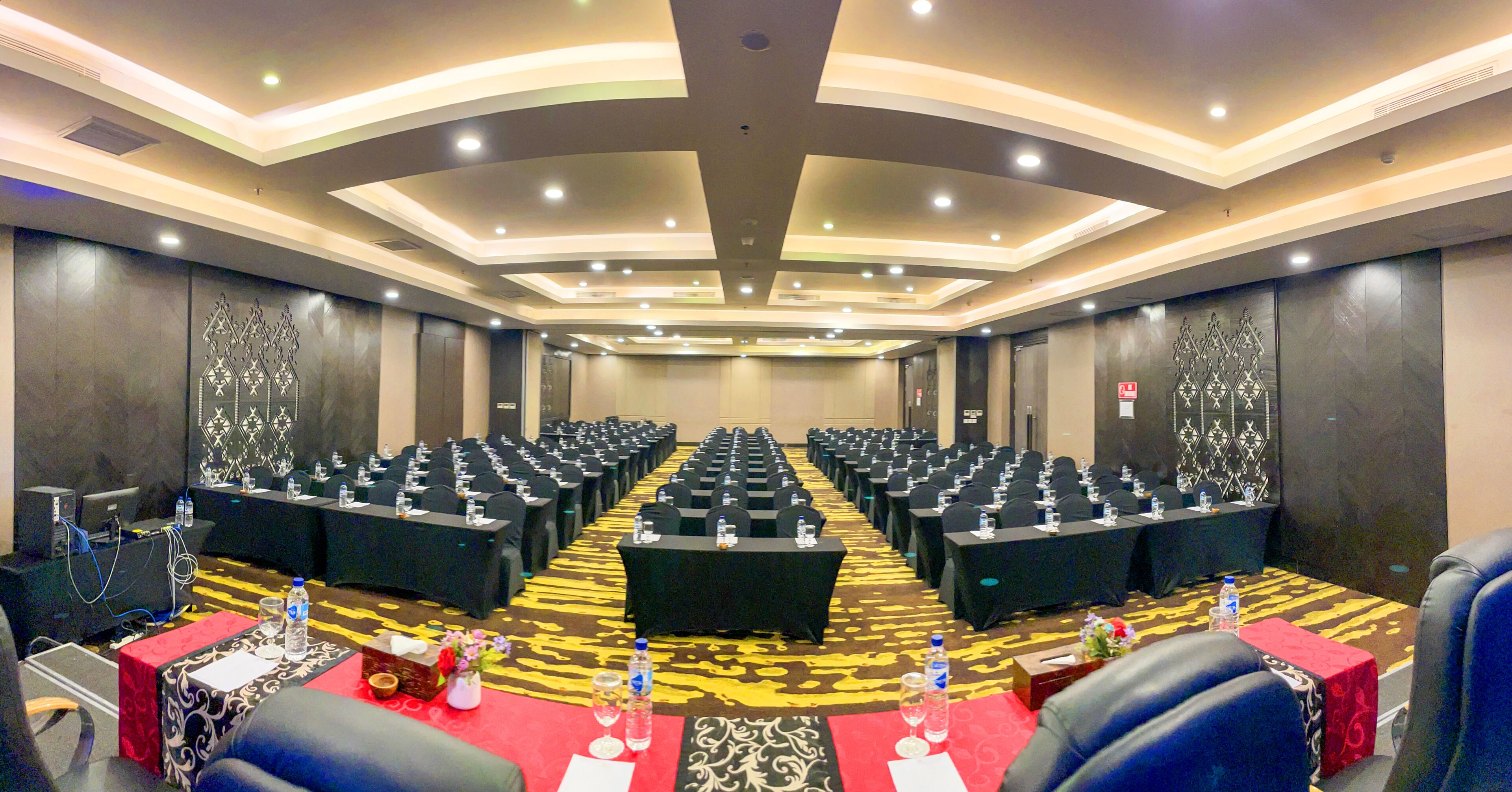 Un salón de conferencias con filas de mesas y sillas, equipado con botellas de agua y tarjetas de identificación.