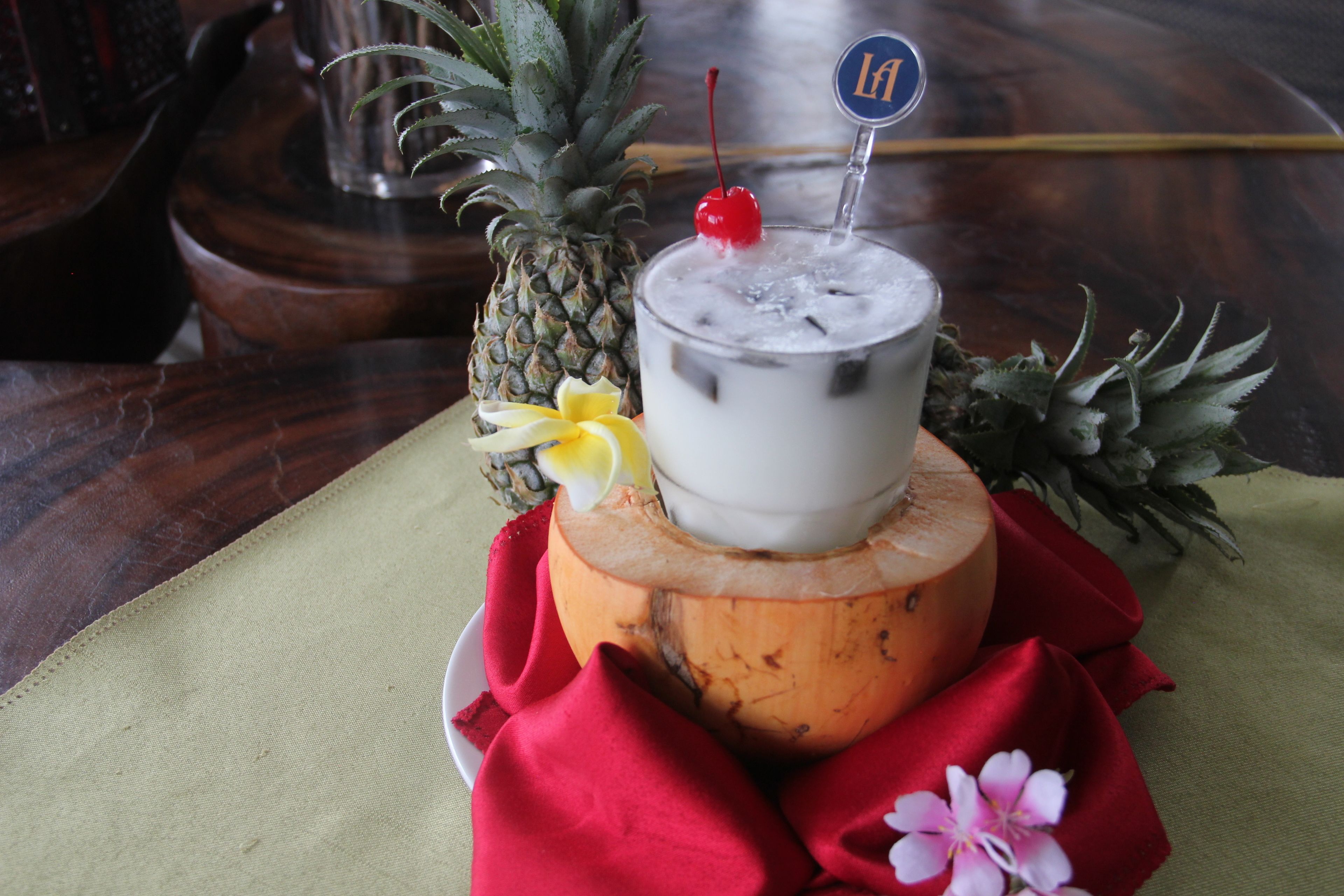 A tropical drink on a wooden base with a red napkin and a pineapple.