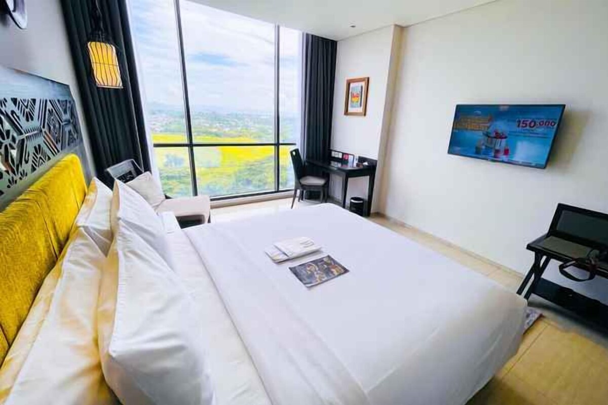 Ein Hotelzimmer mit einem großen Bett, einem Schreibtisch, einem Sessel, einem Fernseher und Blick auf die Stadt.