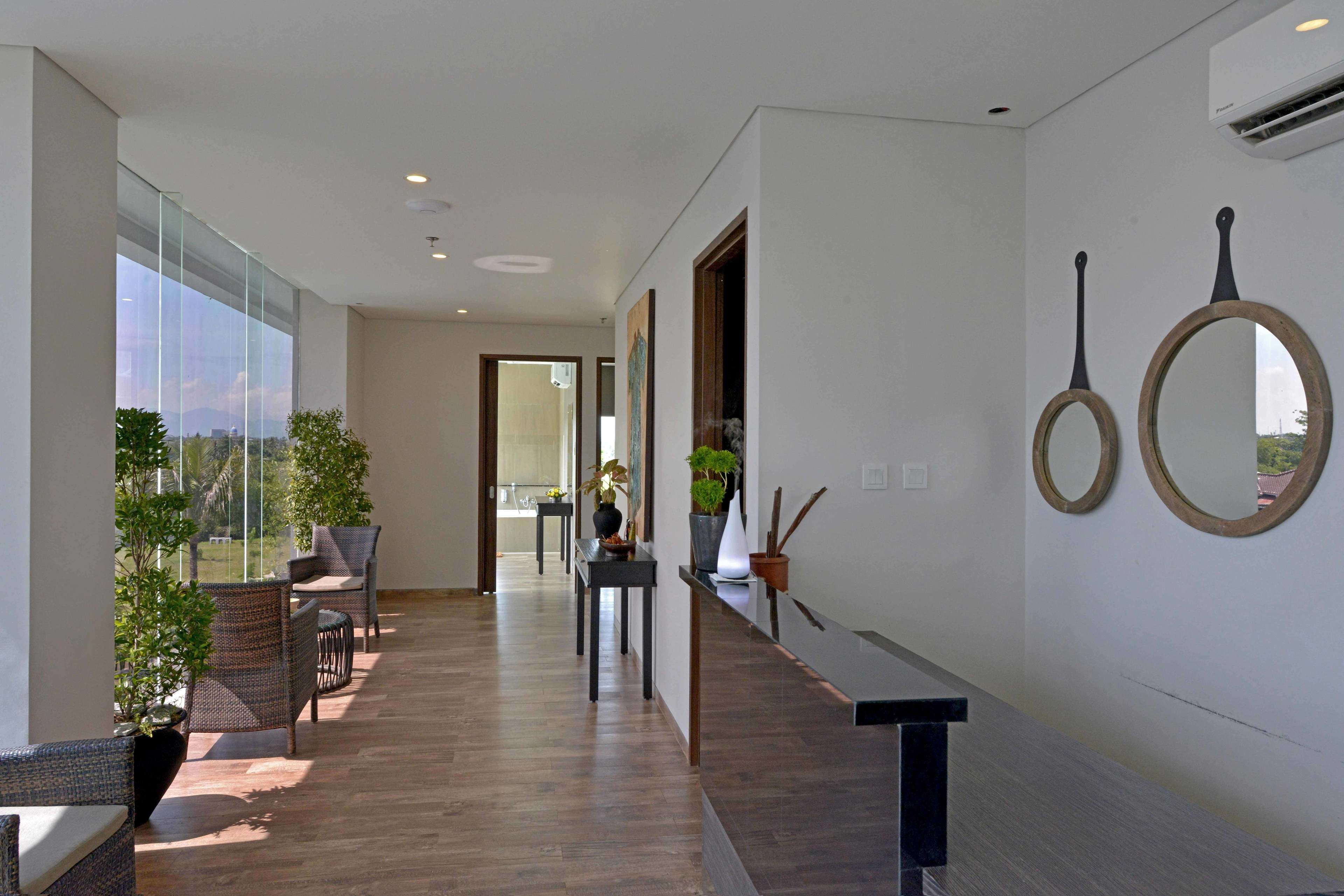Un couloir d’hôtel moderne avec un plancher en bois, des murs en verre et des plantes en pot.