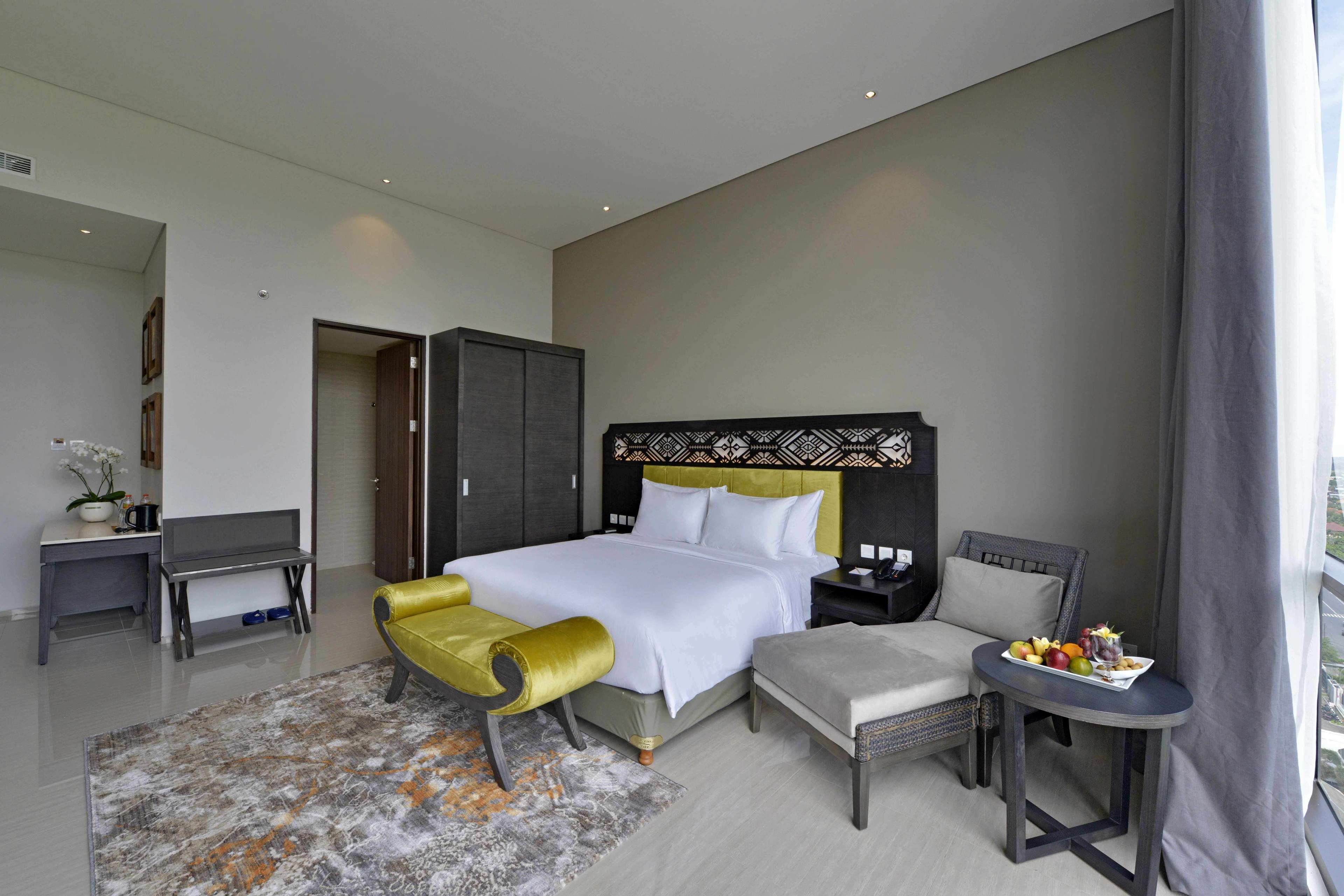 Una habitación de hotel moderna con una cama grande, una mesita con fruta, un sofá y un escritorio con una computadora.