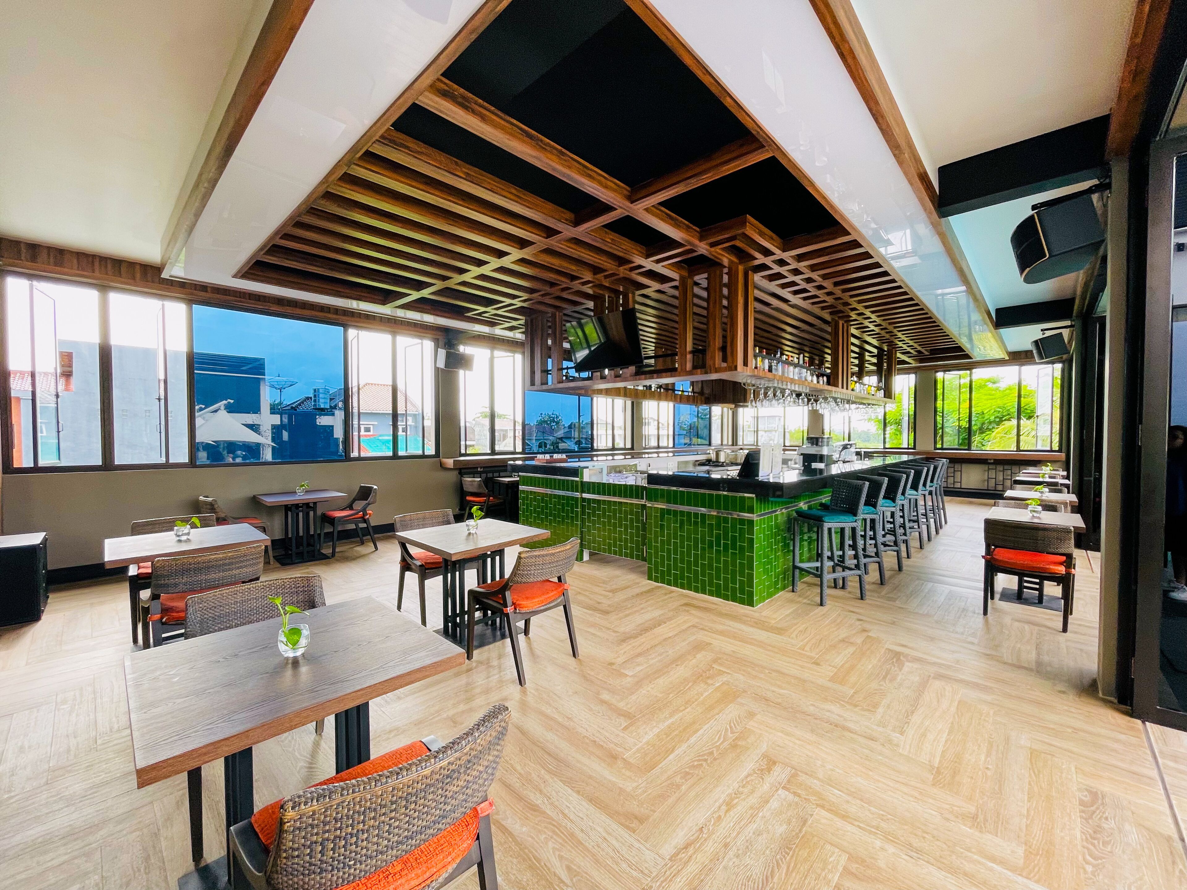 Un restaurant moderne avec un plafond en bois, de grandes fenêtres et un bar au décor verdoyant.