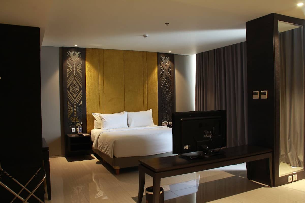 Ein modernes Hotelzimmer mit einem großen Bett, einem Flachbildfernseher, einer Wand mit Holzvertäfelung und einem dunklen Vorhang.