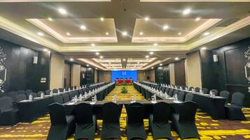 A conference room with rows of tables and chairs, a carpeted floor, and a blue screen at the front.