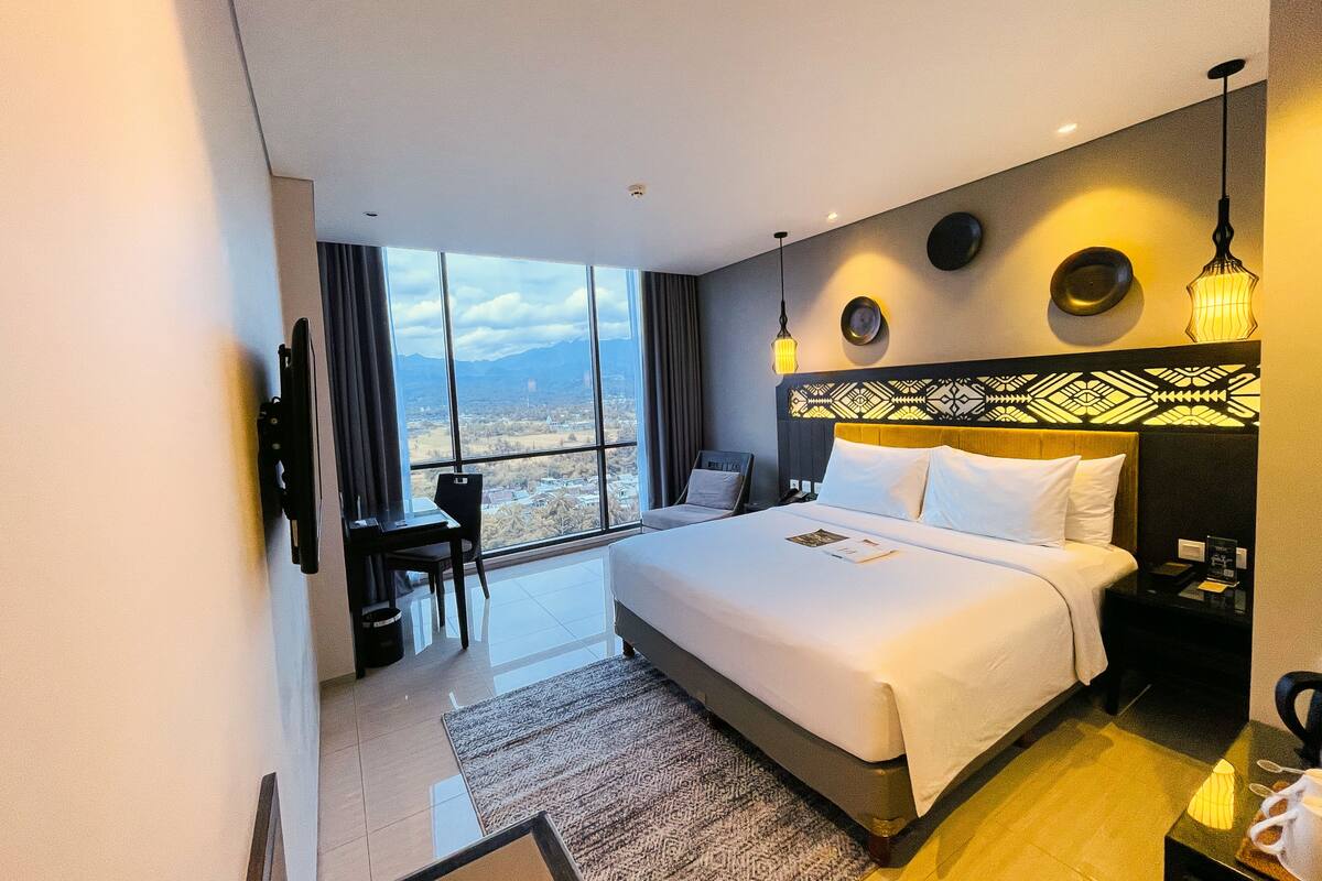 Ein Hotelzimmer mit einem großen Bett, einem Schreibtisch, einem Stuhl und Blick auf die Stadt.