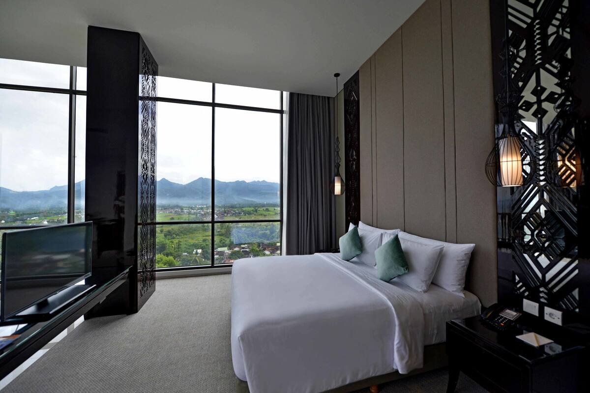 Ein Hotelzimmer mit einem großen Bett, einem Fernseher und Bergblick durch große Fenster.