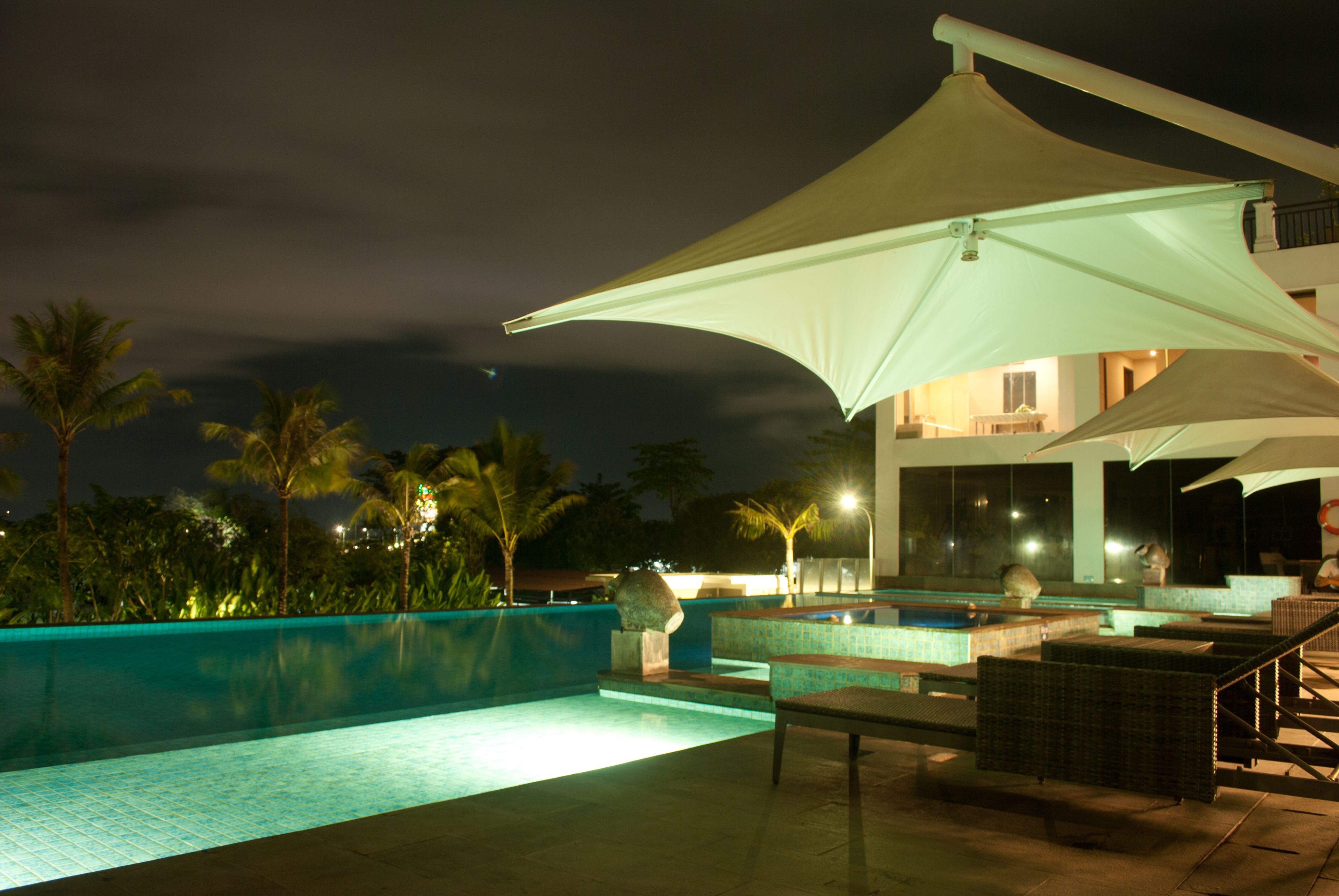 A nighttime pool area with a large umbrella, lounge chairs, and a view of the surrounding landscape.