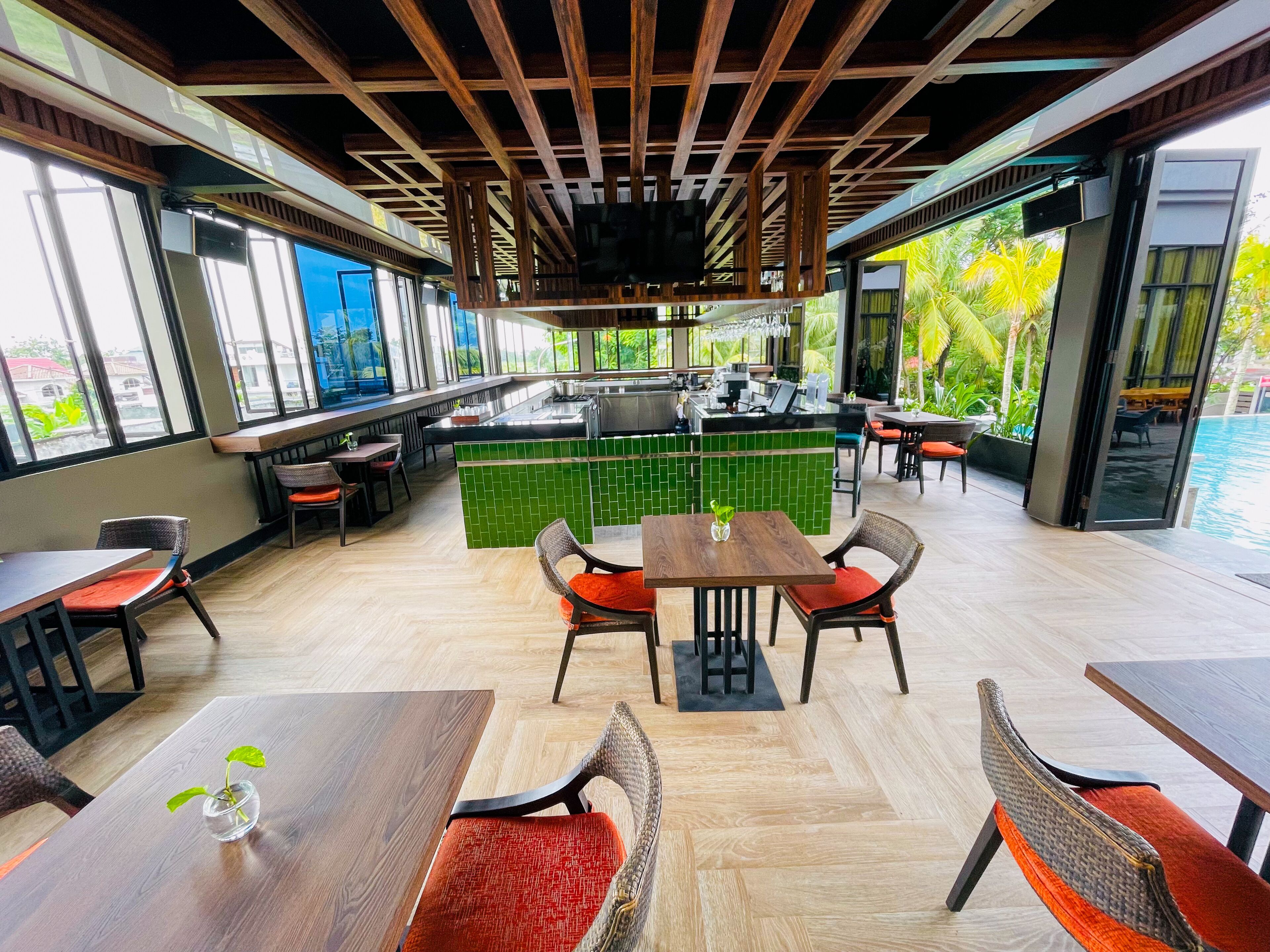 A modern restaurant with a bar area, wooden ceiling, and large windows offering a view of the outdoors.