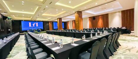 A conference room with long tables, chairs, and a large screen displaying 'Lombok Astoria Hotel'.
