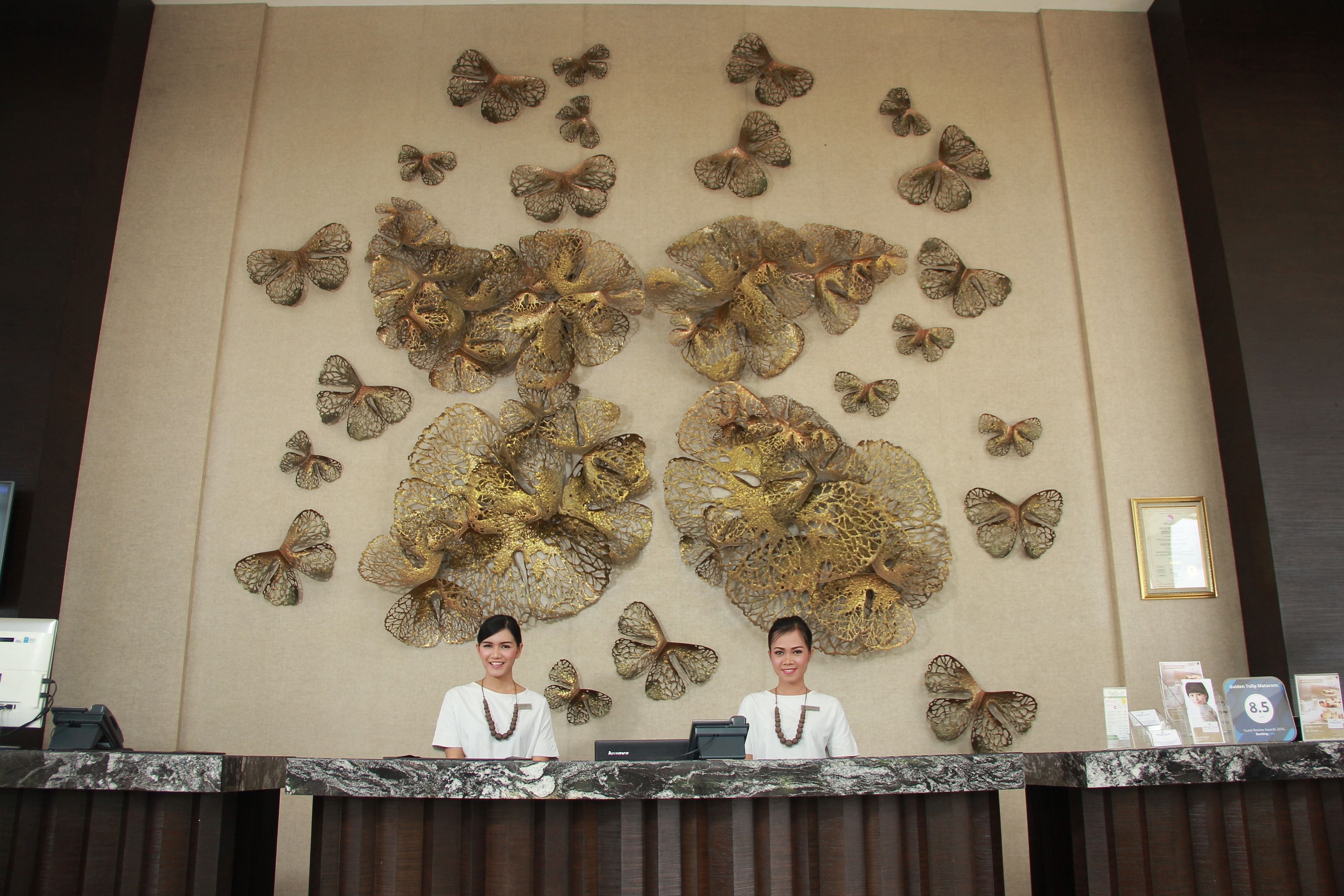 A reception desk with two staff members, a wall with butterfly decorations, and a framed picture on the wall.