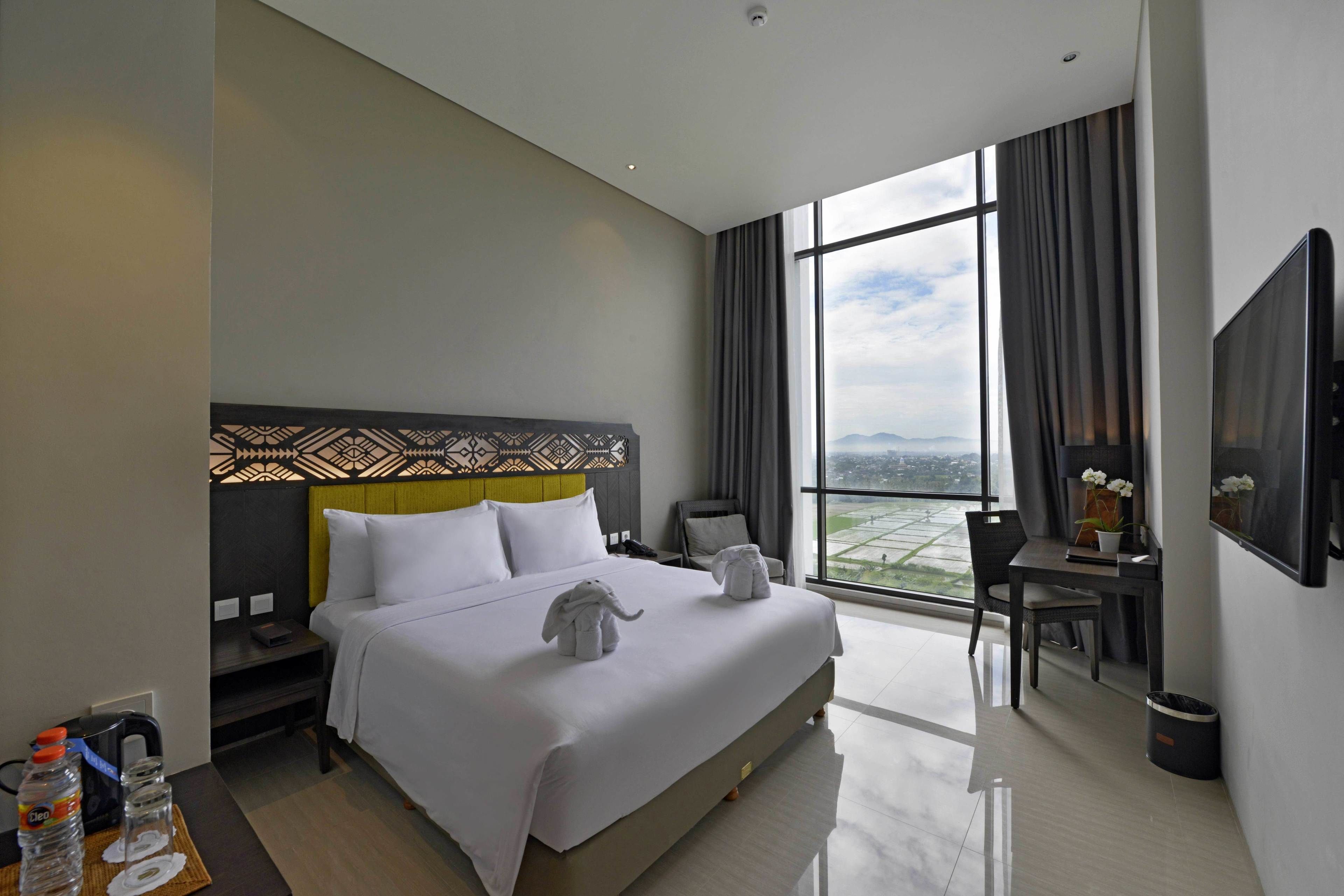 A modern hotel room with a large bed, a desk, and a view of the city.