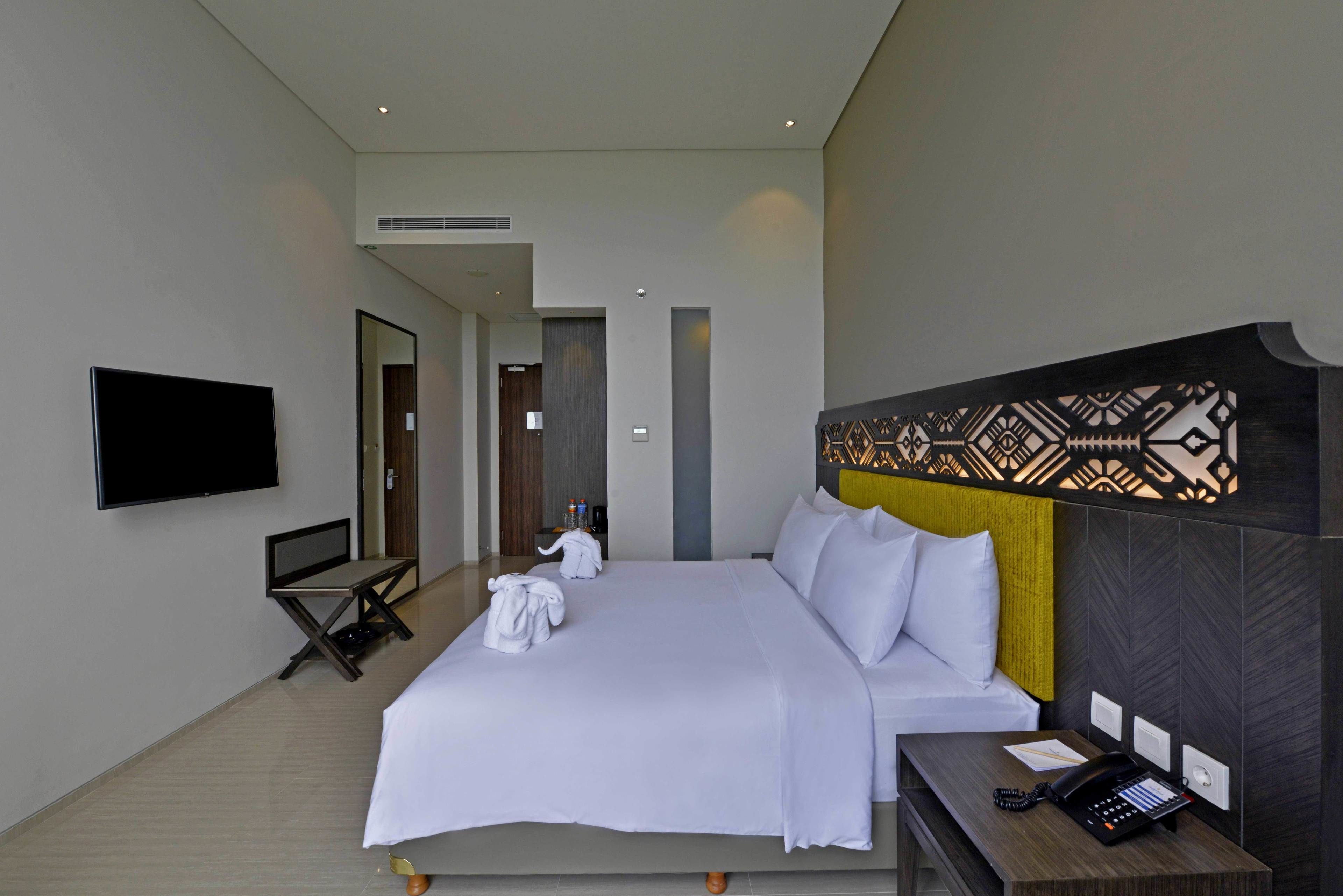 Une chambre d’hôtel moderne dotée d’un grand lit, d’un téléviseur à écran plat, d’un bureau avec un téléphone et d’une tête de lit décorative.