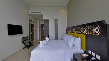 Une chambre d’hôtel moderne dotée d’un grand lit, d’un téléviseur à écran plat, d’un bureau avec un téléphone et d’une tête de lit décorative.
