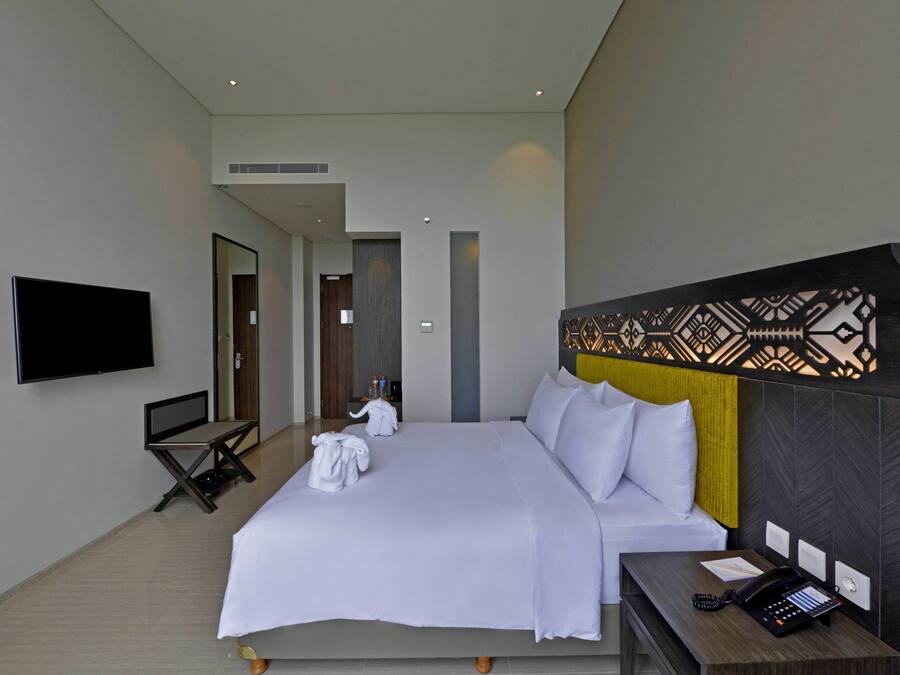 Une chambre d’hôtel moderne dotée d’un grand lit, d’un téléviseur à écran plat, d’un bureau avec un téléphone et d’une tête de lit décorative.