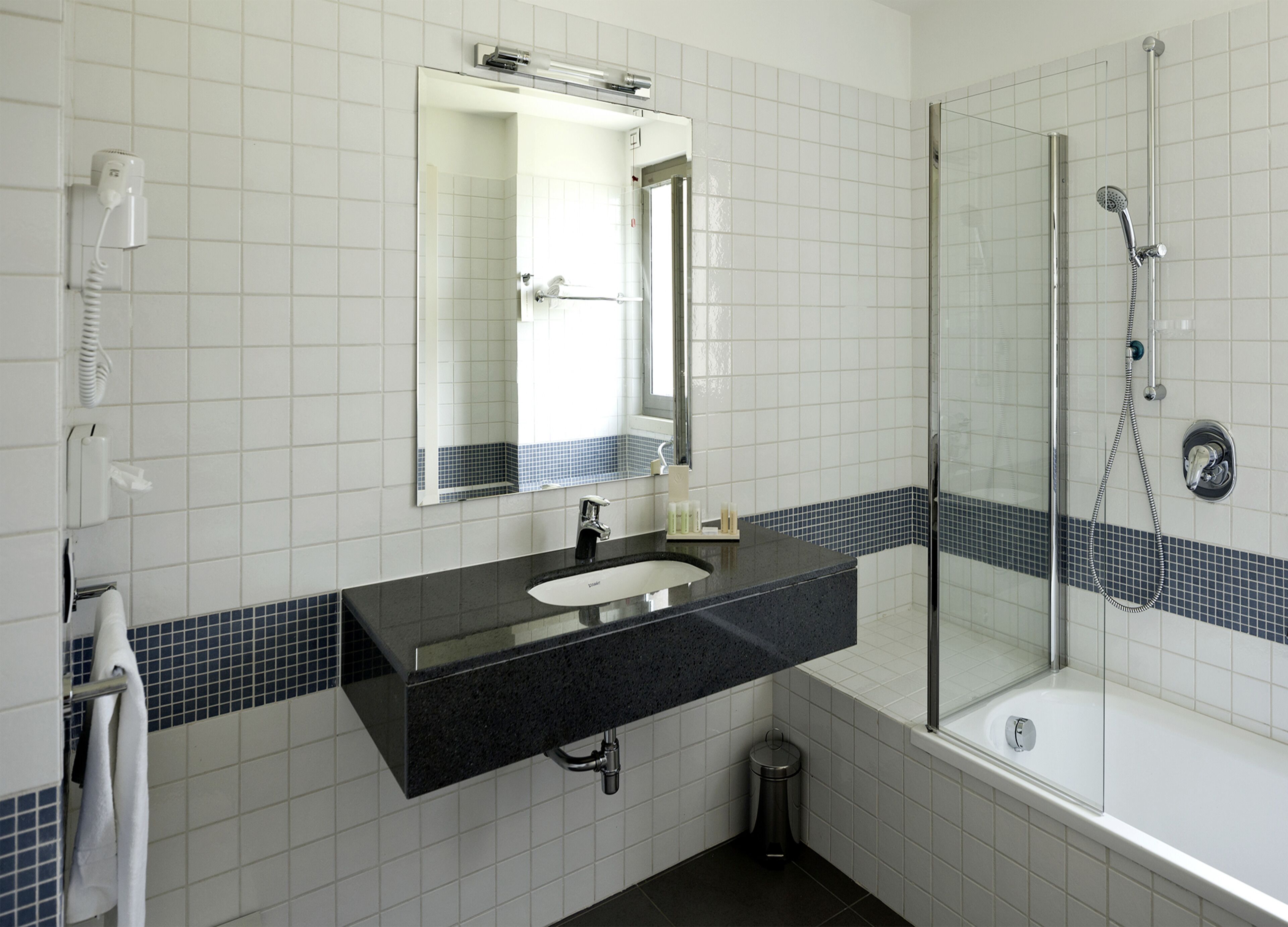 Un baño con lavabo negro, azulejos blancos, cabina de ducha de vidrio y toallero.