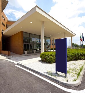 A modern building with a covered entrance, large windows, and a flag in the background. - Inn Naples Airport (Gricignano d'Aversa)
