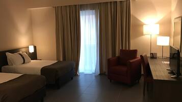 Habitació d'hotel amb dos llits, una taula de treball amb cadira, televisió i una finestra gran amb cortines.
