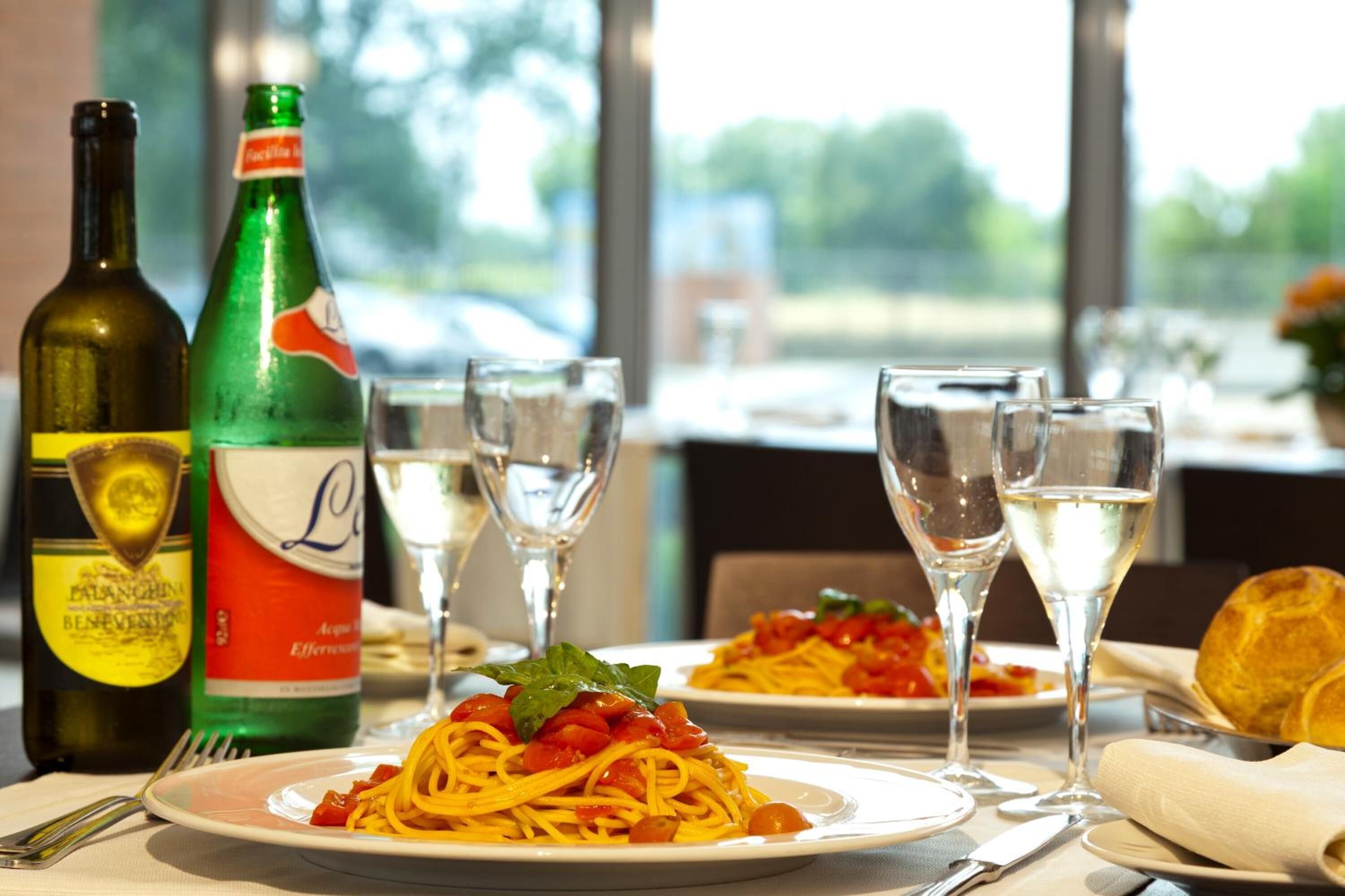 A dining table with plates of spaghetti, wine bottles, and glasses.