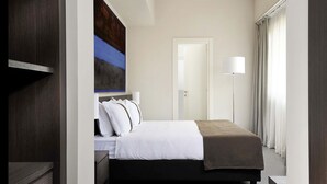 Ein modernes Hotelzimmer mit einem großen Bett, einem Nachttisch, einer Stehlampe und einem Bild an der Wand.