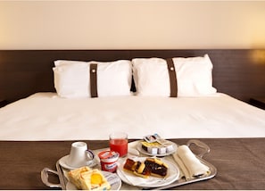 A neatly made bed with white linens and two pillows, a tray with breakfast items including a glass of juice, yogurt, pastries, and a rolled-up napkin. - Inn Naples Airport (Gricignano d'Aversa)