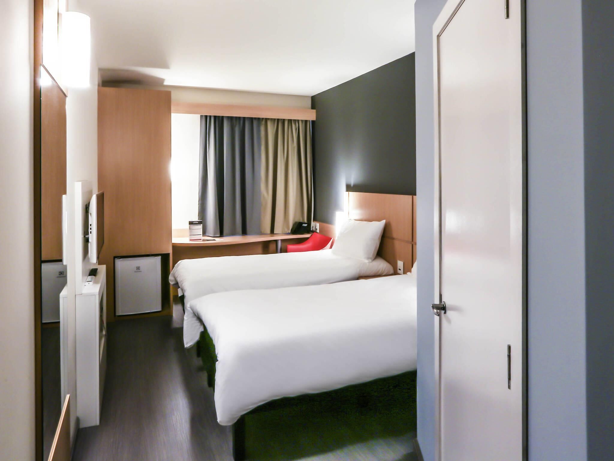 Une chambre d’hôtel avec deux lits, un bureau, une chaise, une télévision et une fenêtre avec des rideaux.
