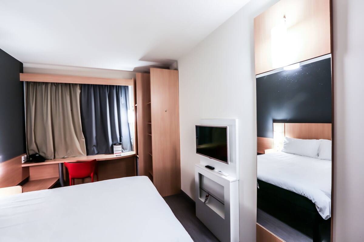 Hotellihuone, jossa on sänky, työpöytä, televisio ja punainen tuoli.