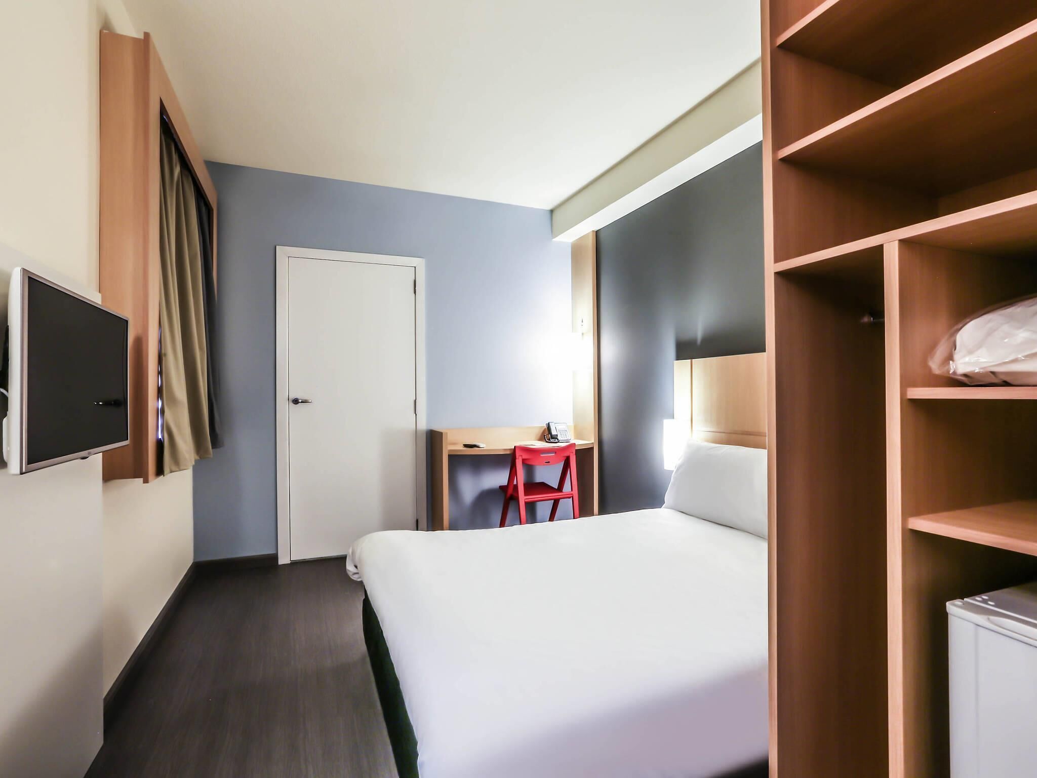 Une chambre d’hôtel comprenant un lit, un bureau, une chaise, une armoire et un téléviseur.