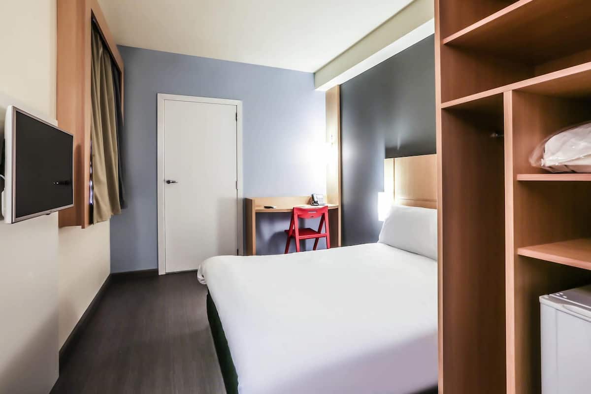Une chambre d’hôtel comprenant un lit, un bureau, une chaise, une armoire et un téléviseur.