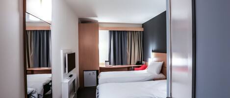 A hotel room with two beds, a desk with a computer, a TV, and a small cabinet.