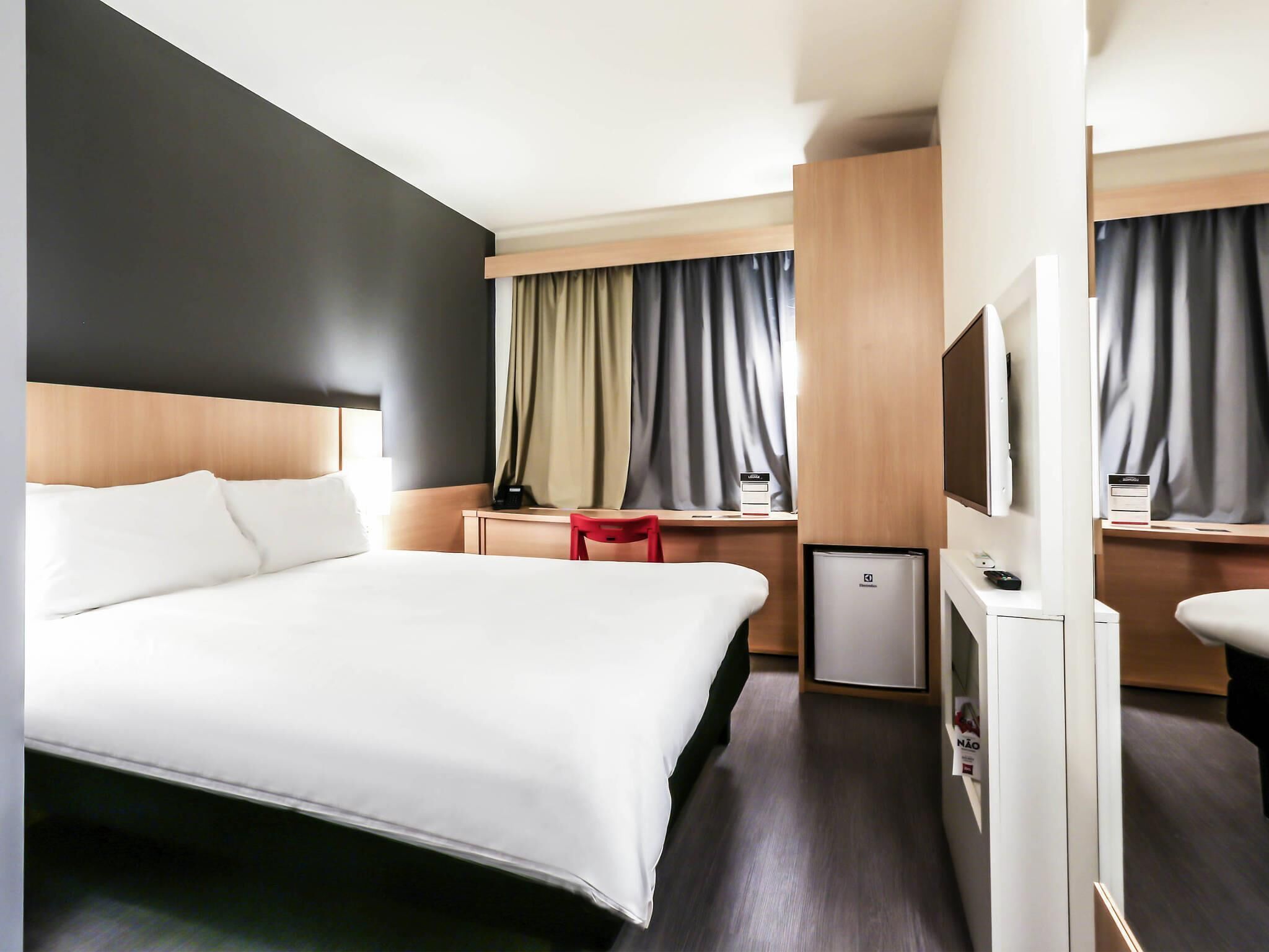 Une chambre d’hôtel équipée d’un lit, d’un bureau, d’une chaise, d’une télévision et d’un mini-bar.