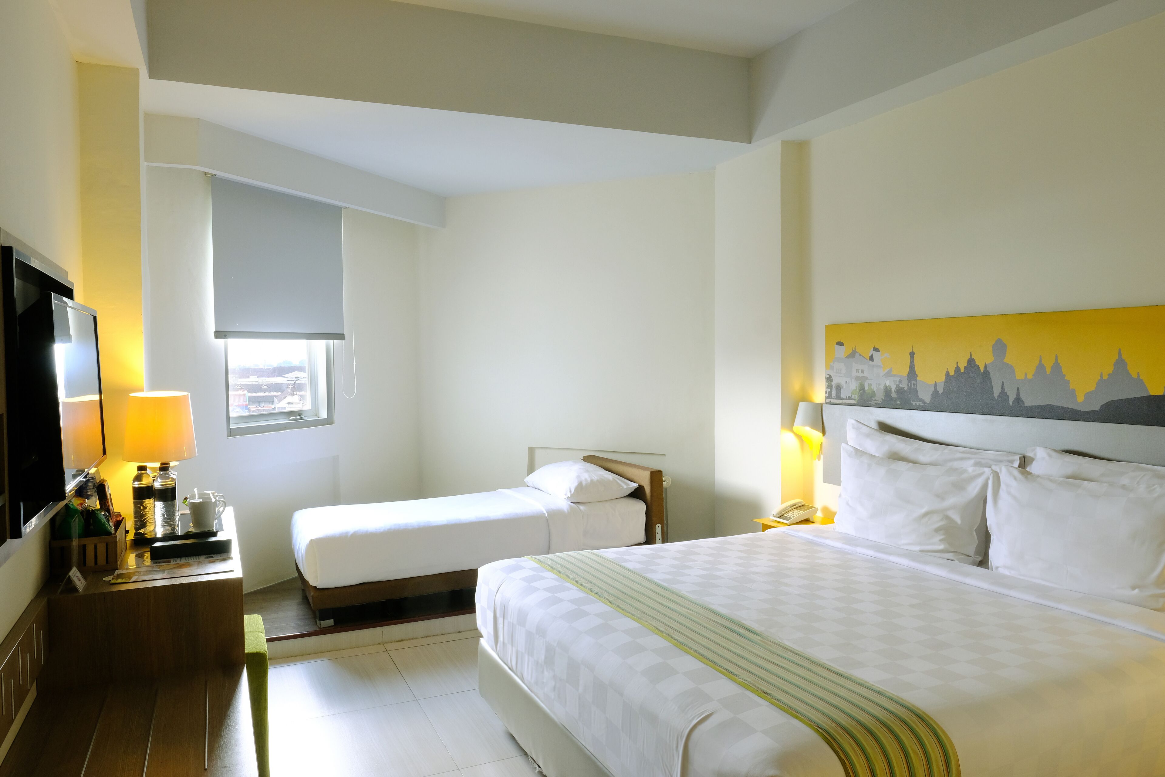 A hotel room with a large bed, a smaller bed, a desk with a lamp, a TV, and a window with a view.