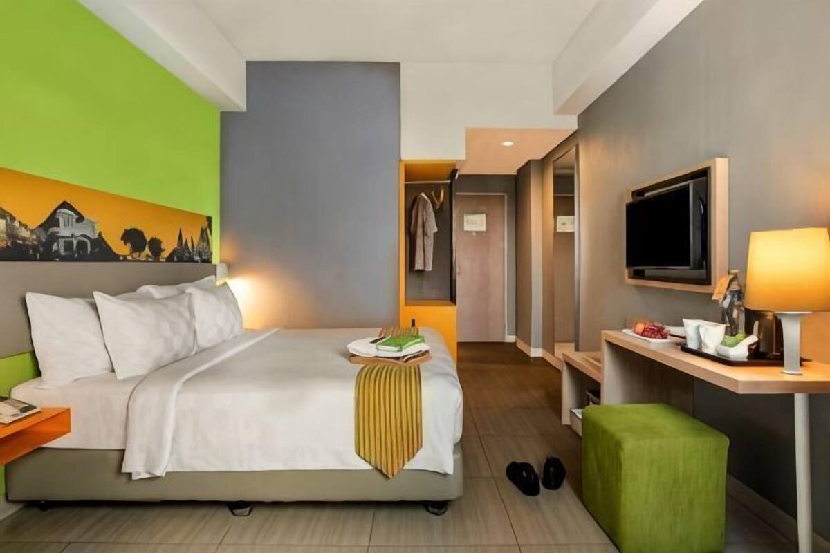 Une chambre d’hôtel avec un lit, un bureau avec une télévision, une chaise et un tableau au mur.