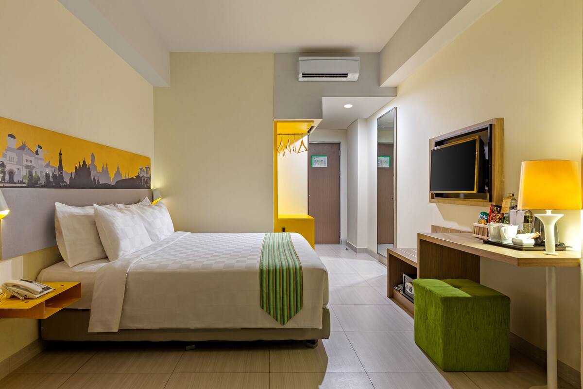 Une chambre d’hôtel avec un lit, une table de chevet, une lampe, une télévision et un tableau au mur.