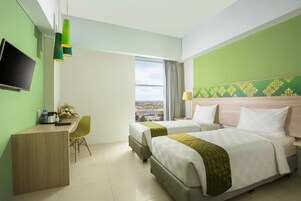 Habitación de hotel con dos camas, un escritorio, un televisor y vistas a la ciudad.