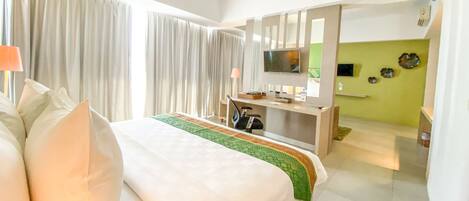 Una habitación de hotel con una cama grande, un escritorio con computadora, un televisor y una pared verde.