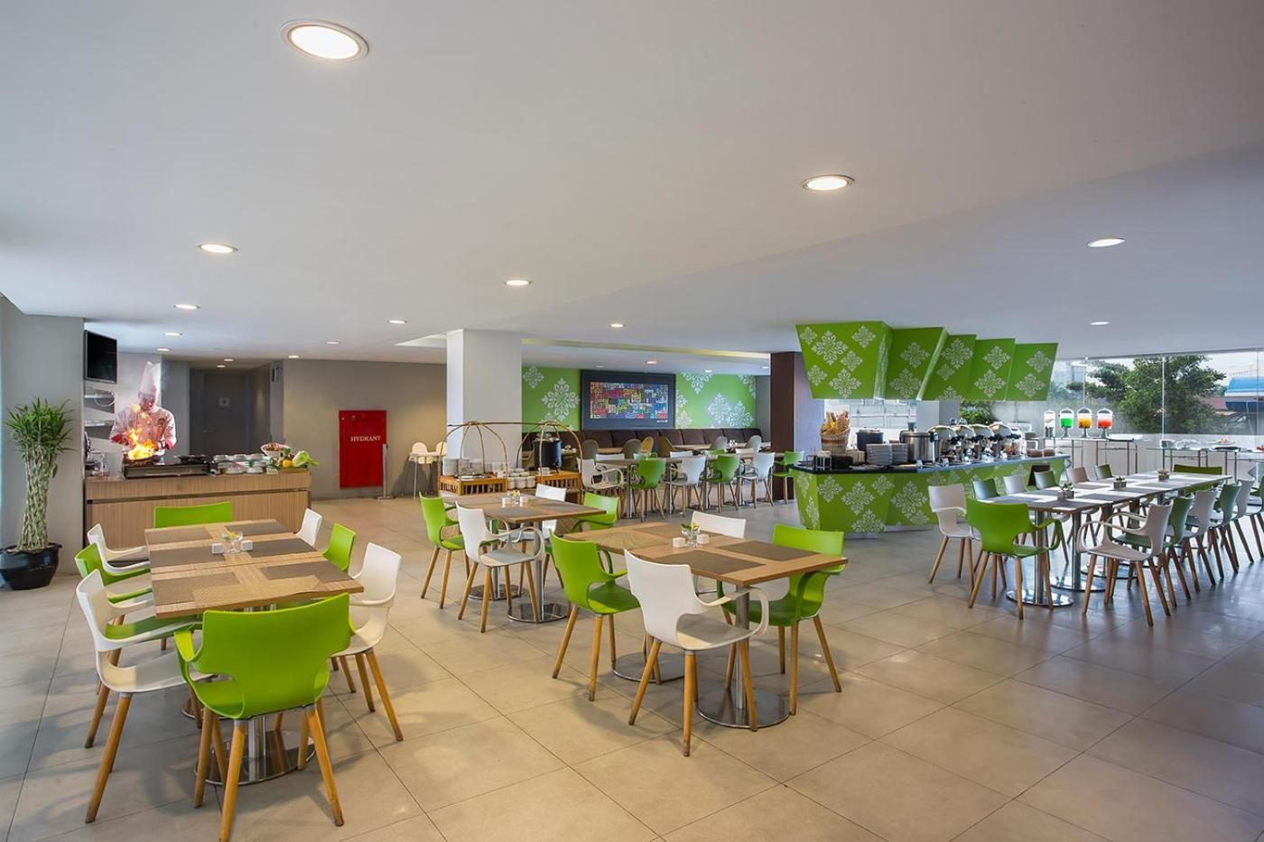A modern restaurant with multiple dining tables and chairs, a kitchen area with a chef, and a bar counter.