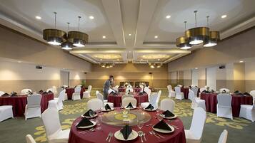 A banquet hall with round tables set for dining, white chairs, and a central serving area.