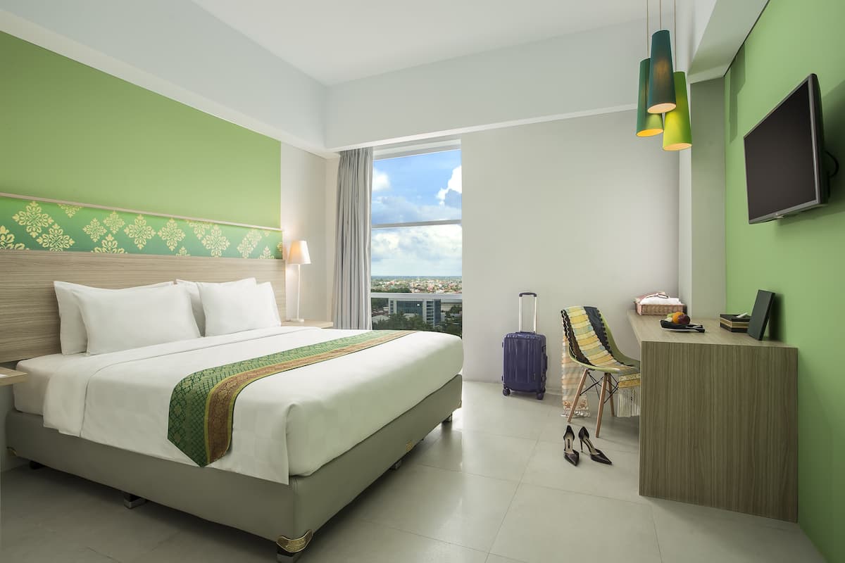 A hotel room with a bed, a desk, a chair, a suitcase, and a TV.