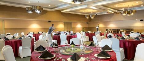 A banquet hall with round tables covered in red tablecloths, white chairs, and black napkins.