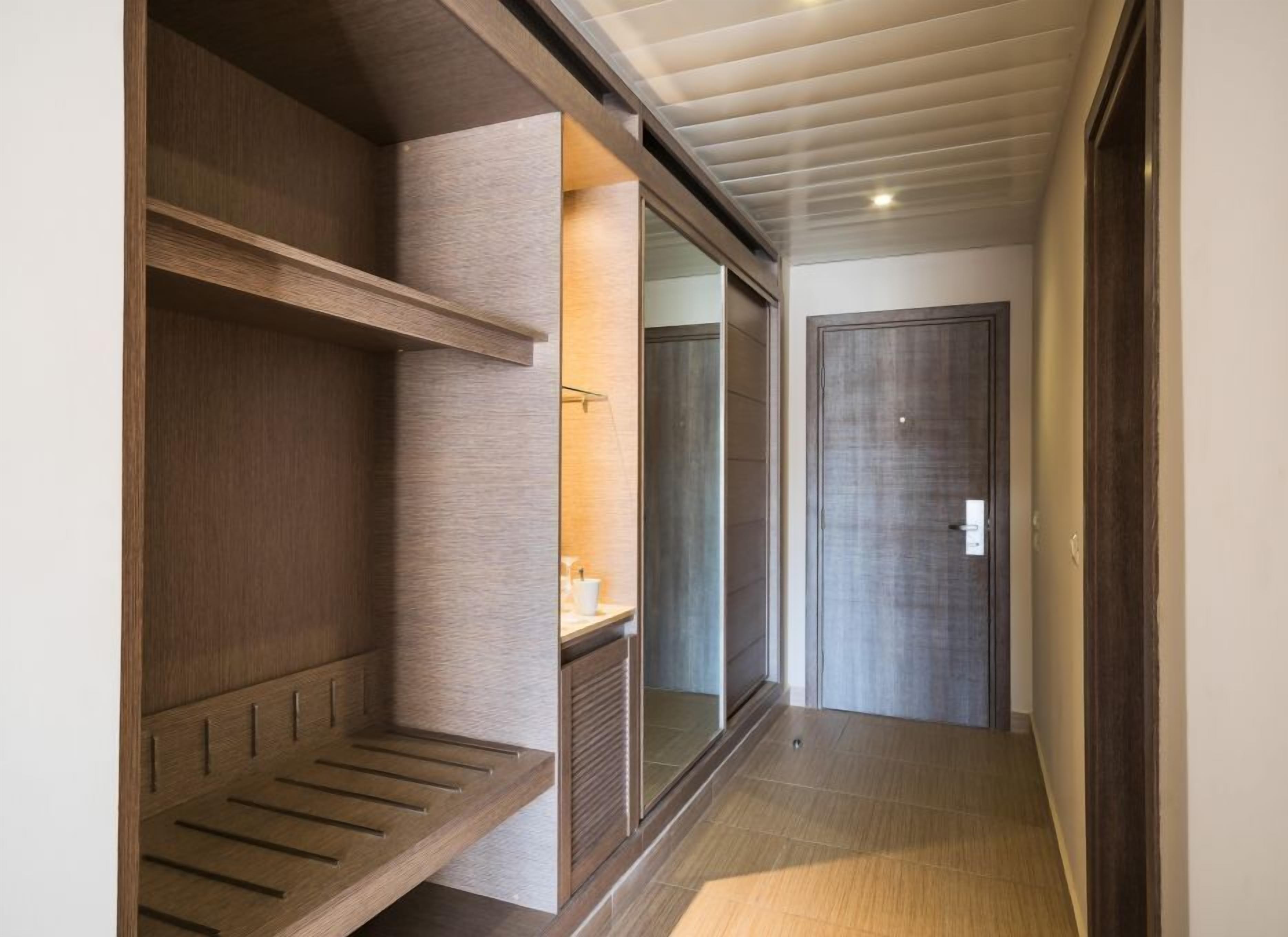 Un couloir avec un banc en bois, un miroir et une porte.