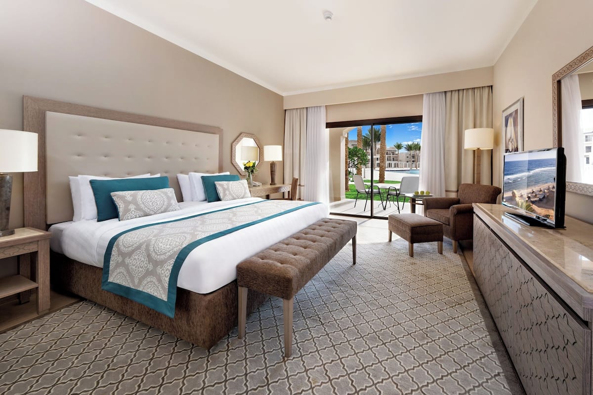 A hotel room with a large bed, a desk, a chair, a bench, and a TV.