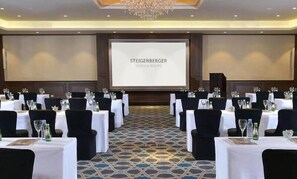 A conference room with tables set for a meeting, a projector screen displaying 'STEIGENBERGER HOTELS & RESORTS', and a chandelier. - Steigenberger Alcazar (Sharm El Sheikh)