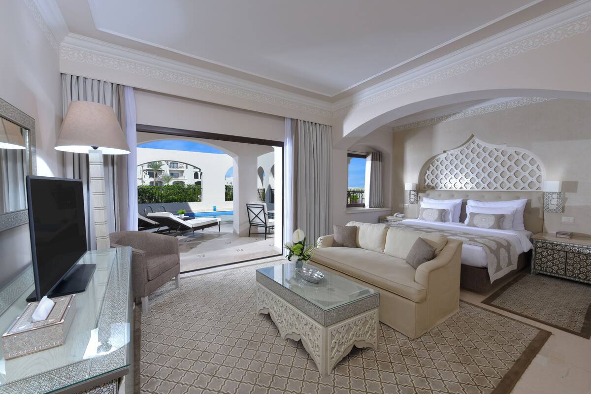 A hotel room with a bed, sofa, TV, and a glass coffee table.